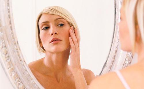 Блондинката внимателно изследва кожата в ъглите на очите в огледало