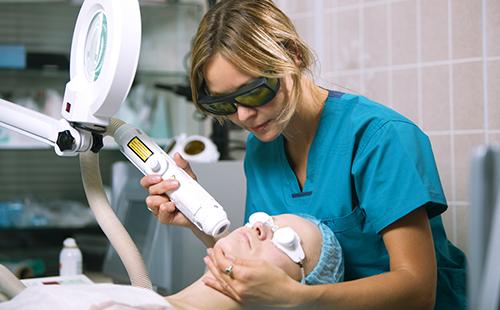 Козметикът третира лицето на пациента с лазер