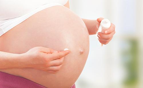 Бременната жена прилага крем върху корема