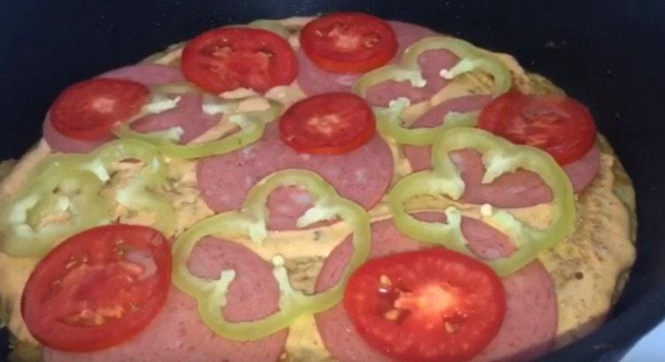 Намазваме картофената си пица със сос и разпределяме пълнежа: наденица, черен пипер, домати.