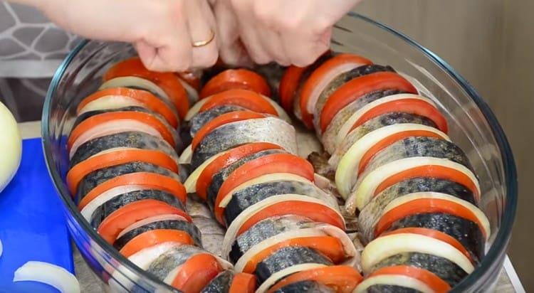 В намазнена форма с растително масло наредете парчетата риба, като ги редувате с резенчета лук и домати.