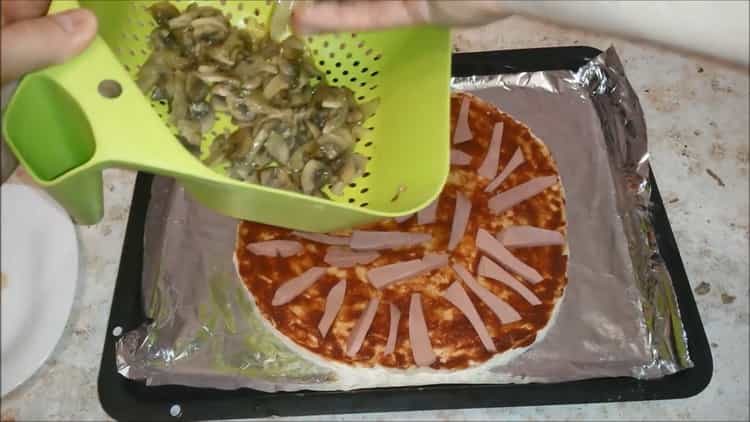 За да приготвите пица с наденица и сирене, сложете пълнежа върху тестото